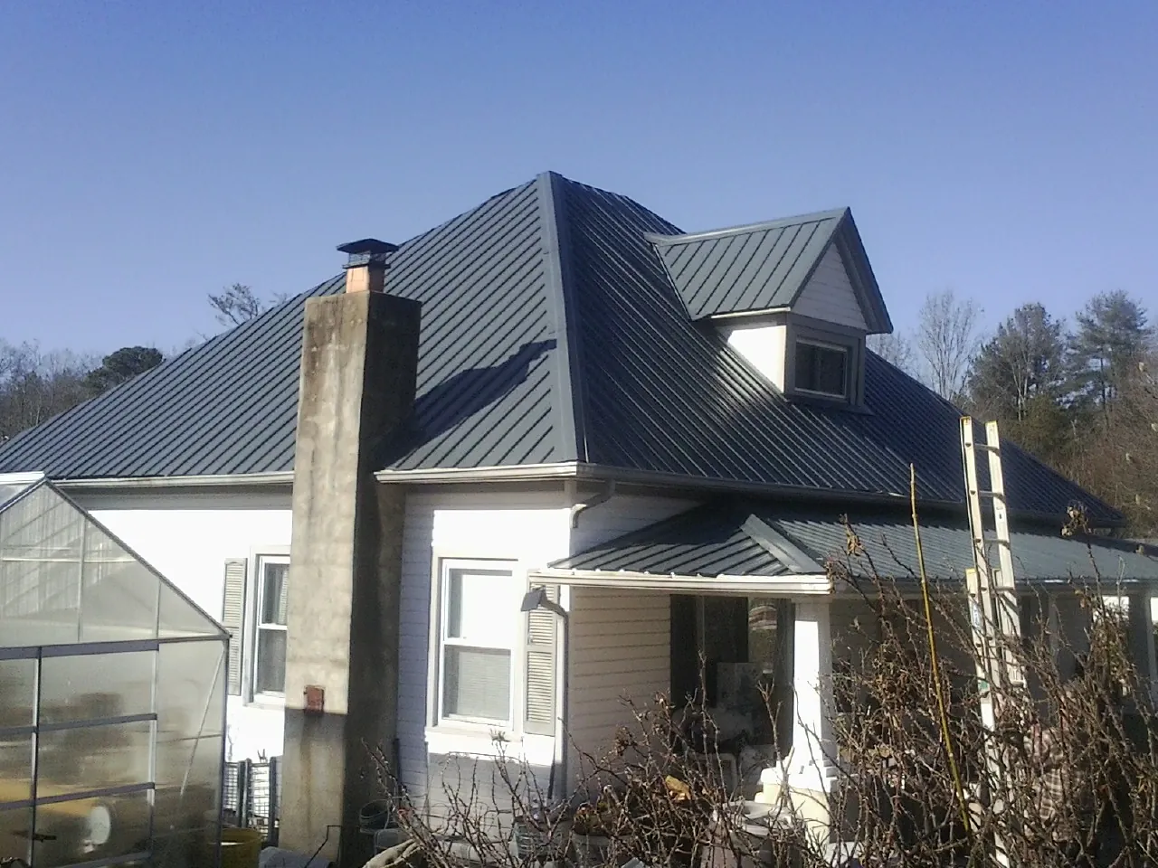 Dark blue standing seam metal roof on a white farmhouse with dormer — Slate & Tile Roof Repair by Roofing Brothers in Coltons Point