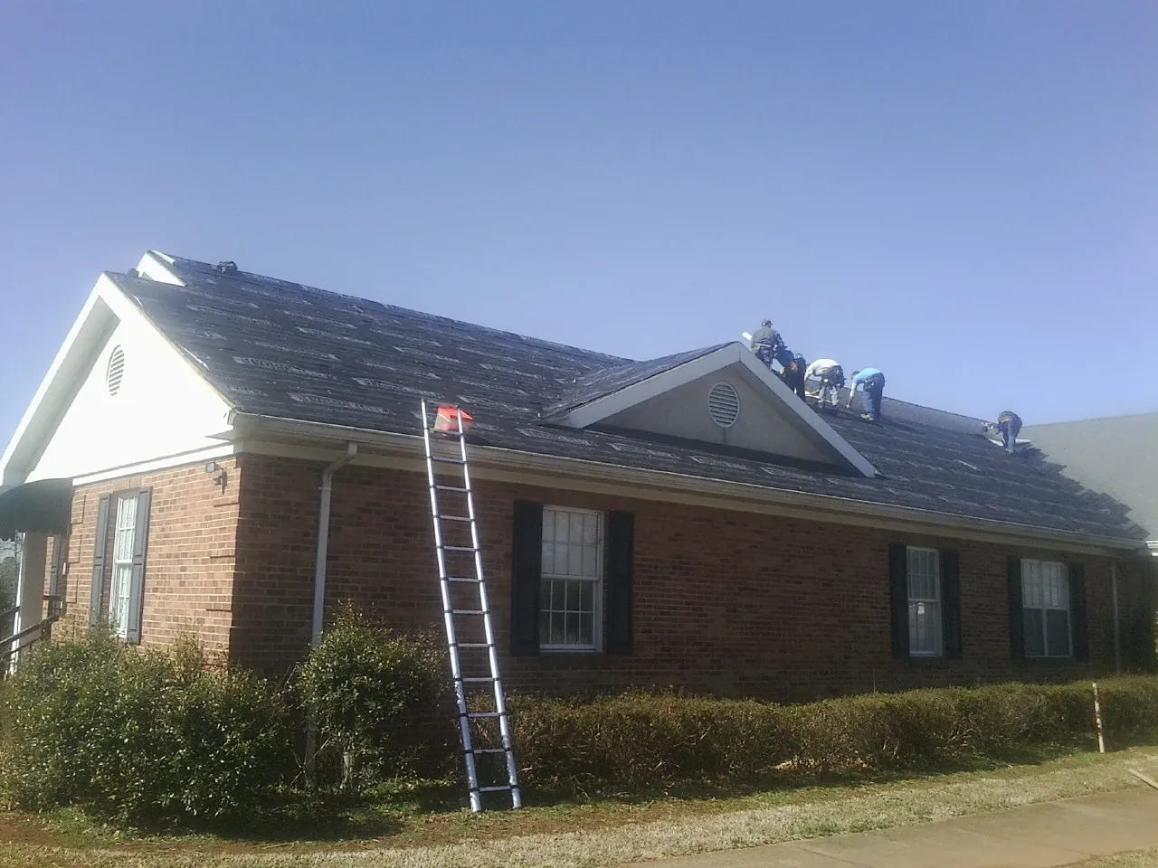 Crew tearing shingles off a brick ranch roof with a ladder set — Emergency Roof Repair work by our crew in Coltons Point
