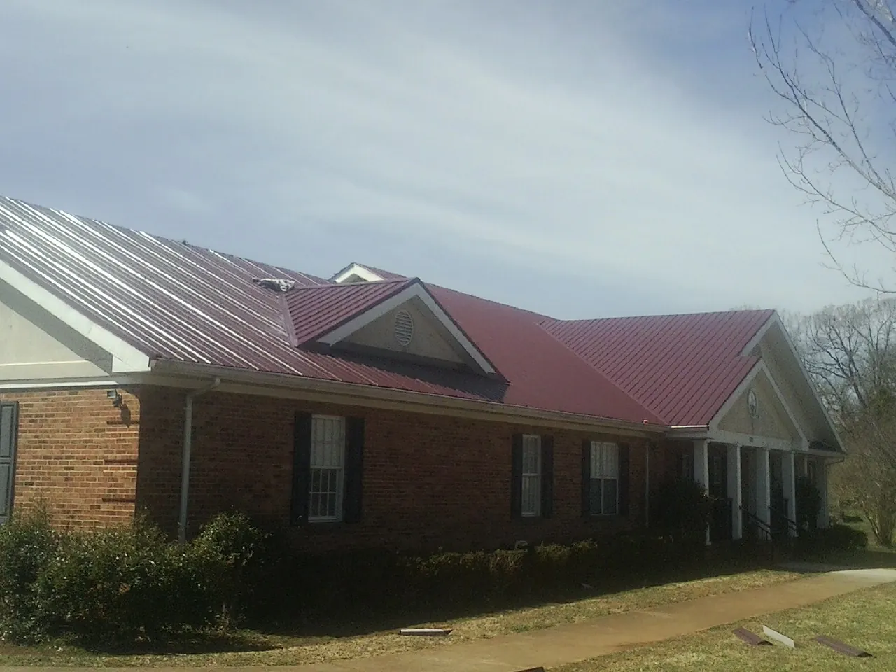 Red metal roof with gabled entries on a long brick building, from a Hail Damage Roof Repair job in Coltons Point