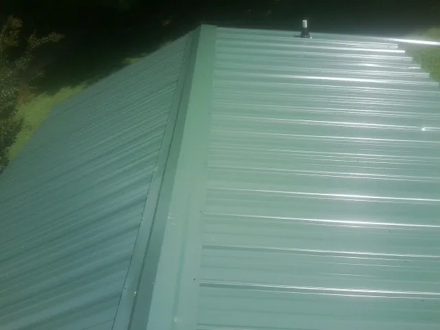 New green metal panels meeting at the ridge of a roof — Flat Roof Repair work by our crew in Coltons Point