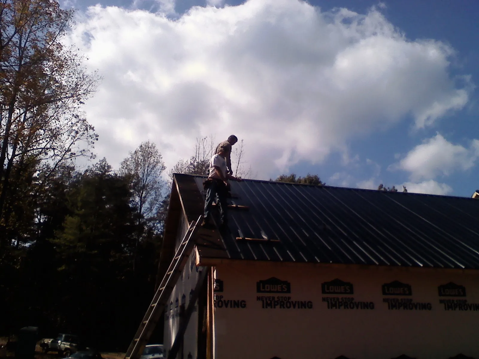Roofer fastening dark metal panels high against a cloudy sky, from a Roof Inspection job in Coltons Point